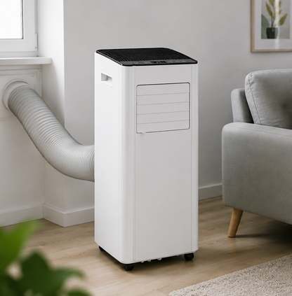 A white portable air conditioner with a black top panel and a flexible gray hose extending from the side, shown in a living room next to a gray sofa.