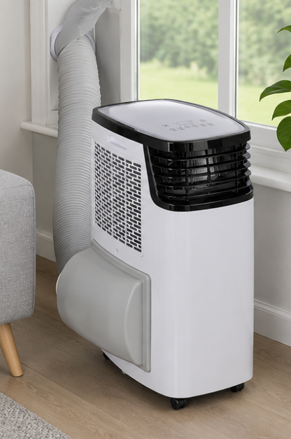 A portable window air conditioner with a white body, black top grille, and gray flexible duct, shown next to a window in a room with light wood floors.